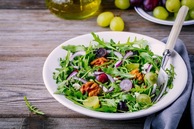 Saladier vert avec roquette noix fromage de chèvre oignon rouge et raisins sur fond de bois