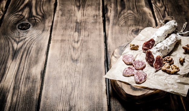 Salami aux noix sur vieux papier sur table en bois.