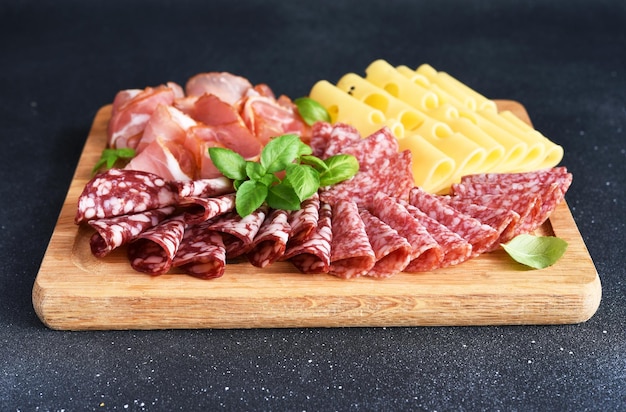 Salami prosciutto au fromage sur une planche carrée en bois sur fond de pierre noire