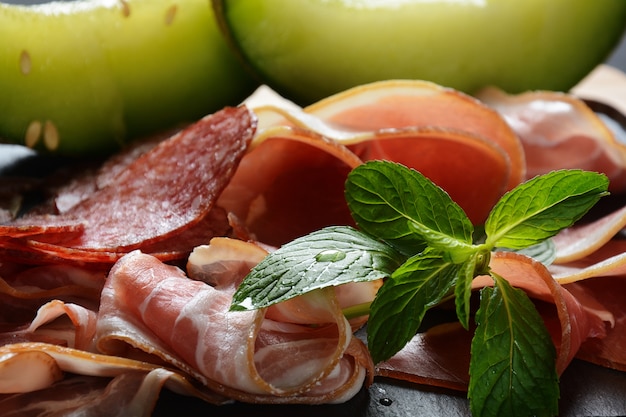 Salami, prosciutto, bacon servi avec melon et menthe sur la planche à découper. Déjeuner italien