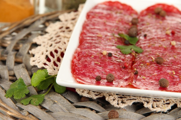 Salami savoureux sur plaque sur berceau en osier isolé sur blanc