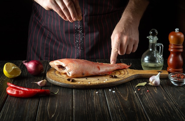 Saler le poisson Sebastes frais dans la cuisine avant la cuisson Le cuisinier saupoudre de sel sur le poisson