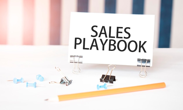 SALES PLAYBOOK signe sur papier sur un bureau blanc avec des outils de bureau Fond bleu et blanc