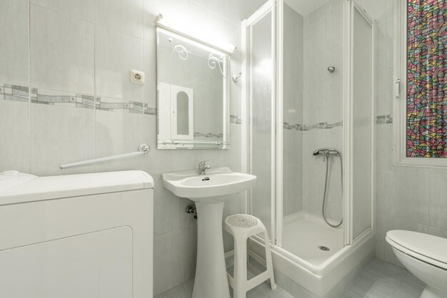 Salle de bain aux tons blancs avec miroir de douche à l'italienne et machine à laver à chargement par le dessus