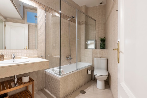 Salle de bain avec lavabo en porcelaine blanche sur miroir sans cadre en marbre crème et cabine de douche avec porte coulissante en verre