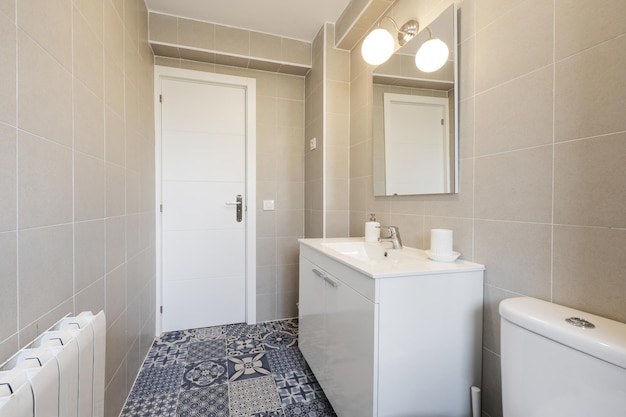 Salle de bain avec des meubles laqués blancs avec un comptoir en résine blanche, des carreaux hydrauliques et un miroir carré sans cadre au mur