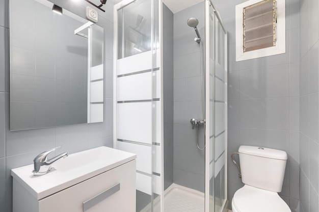 Salle de bain moderne et compacte dans les tons gris et blanc avec douche avec portes en verre cuvette et lavabo