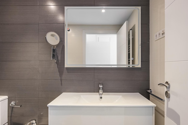 Salle de bain moderne avec toilettes en carrelage gris et grand miroir rectangulaire avec éclairage