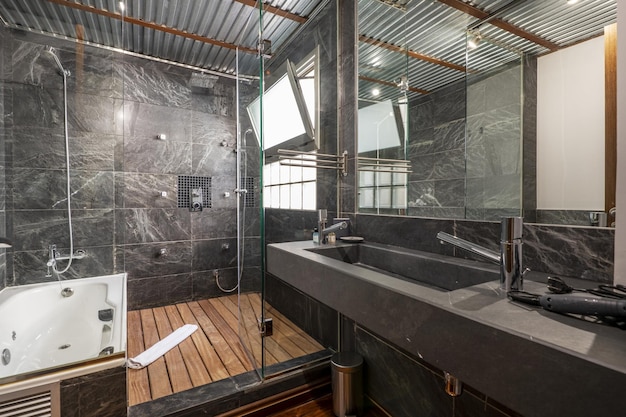 Salle de bain avec paroi en ardoise noire cloison vitrée avec porte et sol en lattes d'acacia porte vitrée vasque en marbre noir et parquet en jatoba