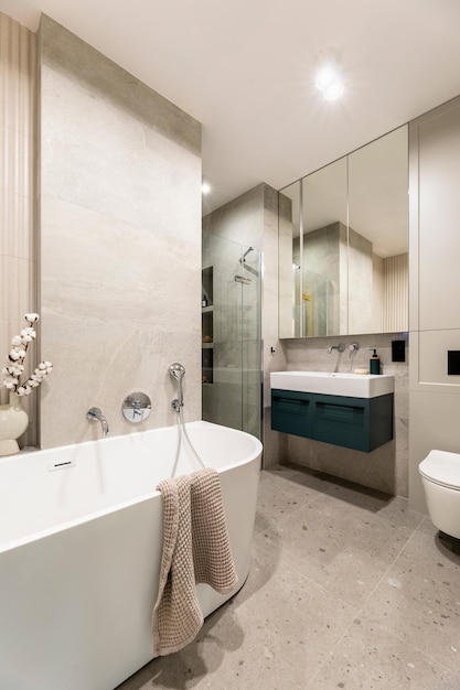 Salle de bains moderne et lumineuse avec mur à lamelles Grande baignoire blanche avec robinet en argent et serviette brune Lavabo avec armoire sombre et morror