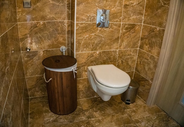 Salle de bains avec panier en bambou avec garniture murale en carrelage marron et toilettes blanches