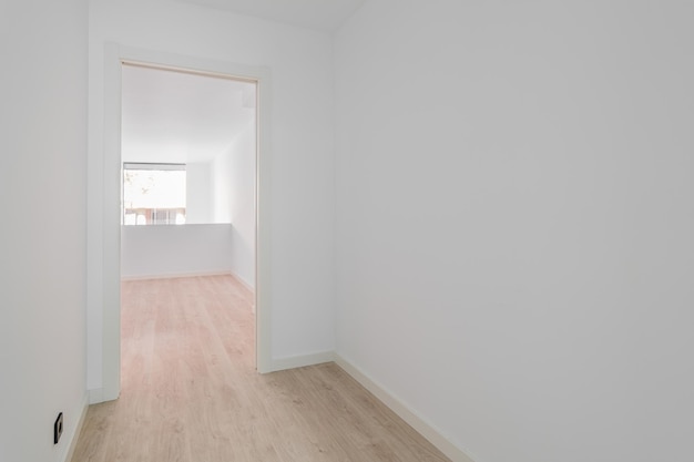 Salle blanche vide après rénovation avec murs blancs, parquet et porte vers une autre pièce