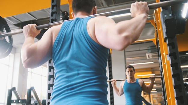 Salle de fitness - homme musclé effectue des squats avec haltères - vue arrière, gros plan