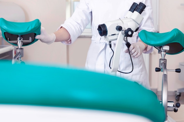 Salle de gynécologie gynécologue chaise équipement docteur femme mains lentille optique microscope