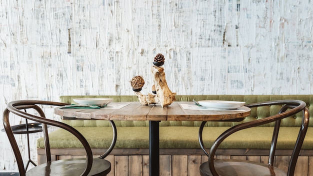 Salle à manger décorée d'un canapé vert, d'une table en bois, d'une chaise en acier noir et d'un papier peint à rayures blanches. Ambiance de restaurant intérieur moderne.