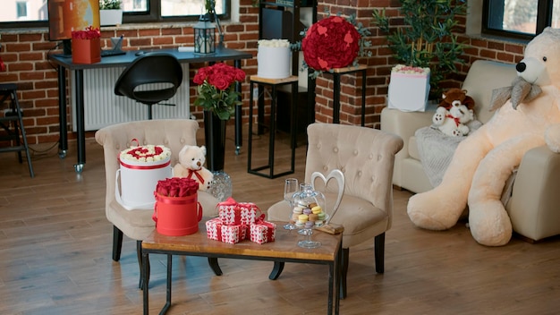 Salle vide avec des cadeaux de luxe surprise pour la Saint-Valentin, un bouquet de roses rouges et un ours en peluche géant sur le canapé. Placement de produit de concept publicitaire saint valentin avec des coeurs, des fleurs et des jouets en peluche.