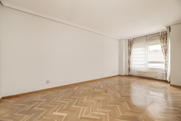 Salle vide avec fenêtre en aluminium blanc avec rideaux fleuris et parquet en chêne