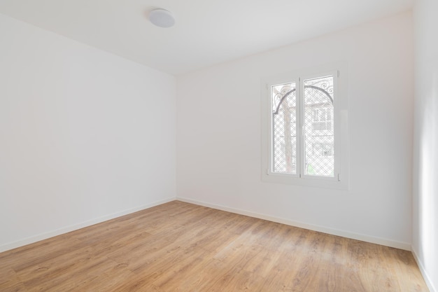 Salle vide avec revêtement de sol stratifié, murs blancs récemment peints et réparation de fenêtres lumineuses et