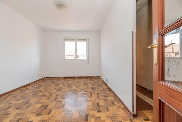 Salle vide avec sol en bois simil sintasol murs peints en blanc et armoire encastrée et porte de la chambre de couleur acajou