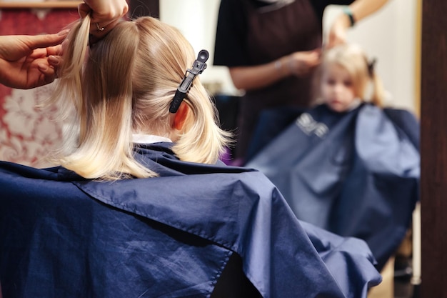 Salon de coiffure coiffeur femme faire une jolie coiffure à la mode pour mignon jeune enfant blond dans un salon de coiffure moderne