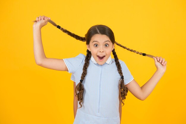 Salon de coiffure. Écolières mignonnes. Filles aux cheveux tressés. Fond jaune d'écolières gaies. Petites filles jouant avec de jolies tresses. De belles écolières. Retour au concept de l'école.