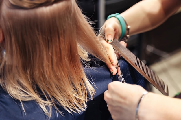 Salon de coiffure gros plan Une femme de coiffure fait une jolie coiffure à la mode pour un jeune enfant blond mignon dans un salon de coiffure moderne