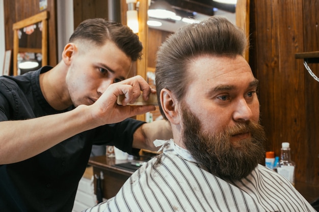 Salon de coiffure, un homme avec un coiffeur à barbe. Beaux cheveux et soins, salon de coiffure pour hommes. Coupe de cheveux professionnelle, coiffure et style rétro. Service Clients. Russie, Sverdlovsk, 12 février 2018