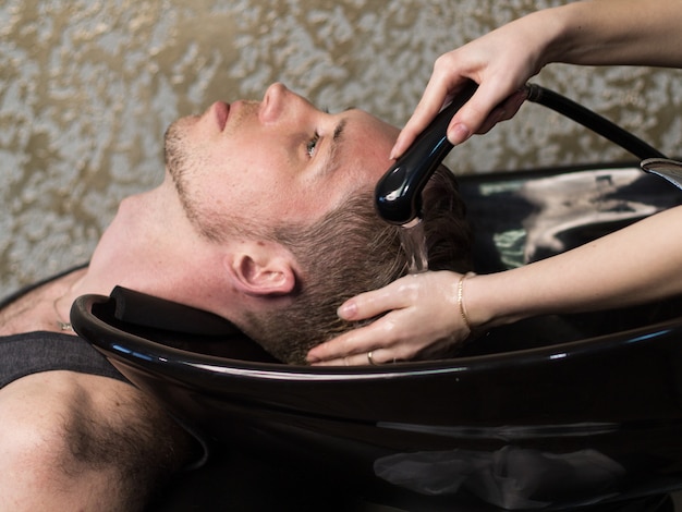 Salon de coiffure. Mains femme, lavage, tête homme, vue côté