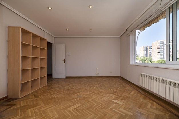 Salon vide avec une bibliothèque en bois colorée sur un mur et une grande fenêtre coulissante sur l'autre