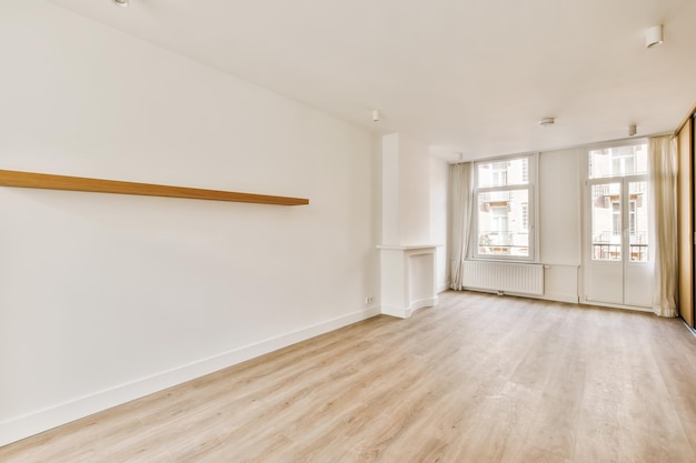 Un salon vide avec parquet et étagères en bois dans le mur est blanc il y a deux fenêtres