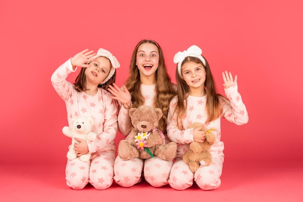 Salut, des enfants surpris agitent les mains en pyjama homewear Filles assises avec des ours en peluche Geste de salutation