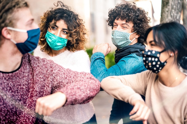 Salutation d'amis multiraciaux avec bosse de coude portant une protection du visage - Focus sur la femme de gauche