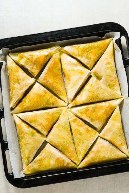 Samosa indien à base de pâte phyllo avec pommes de terre épicées et légumes sur une plaque à pâtisserie, prêt à être cuit au four avec des graines de sésame noir