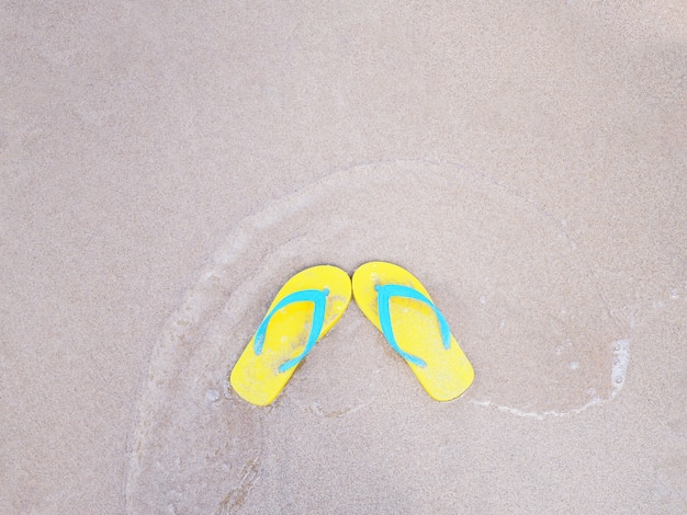 Sandale jaune sur fond de plage d'été de sable beige.