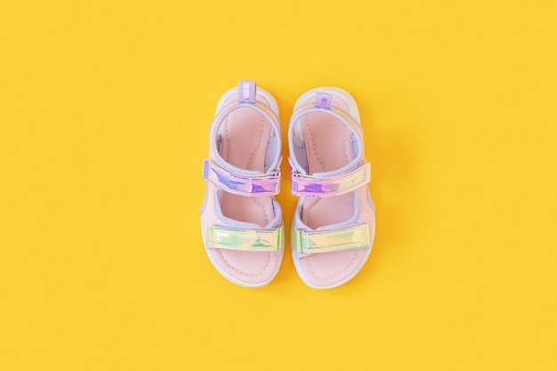 Sandales holographiques élégantes pour enfants sur fond jaune Chaussures d'été mode brillantes Mise à plat Vue de dessus