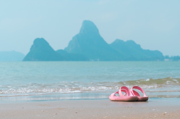 Sandales roses sur la plage avec la montagne dans la mer sont de fond