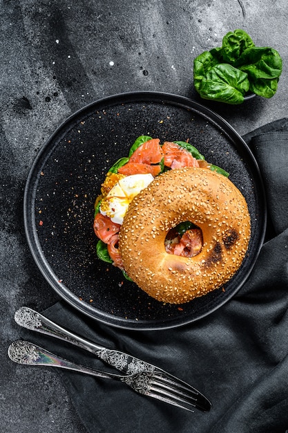 Sandwich au bagel fait maison avec saumon, fromage à la crème, épinards et œuf. Surface noire. Vue de dessus