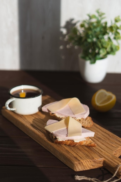 Sandwich au beurre de jambon en tranches et au fromage sur une planche à découper en bois près d'une tasse de thé au citron