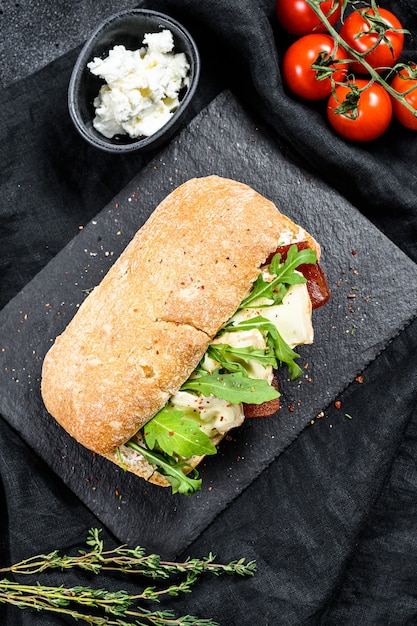 Sandwich au camembert frais, marmelade de poire, ricotta et roquette. Surface noire. Vue de dessus