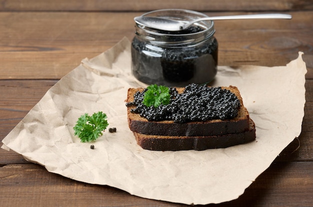 Sandwich au caviar noir sur une tranche de pain de seigle et un pot avec une cuillère, une délicieuse collation sur la table