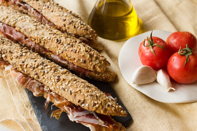 Sandwich au jambon espagnol gros plan avec de l'huile d'olive, de la tomate et de l'ail. Apéritif de la cuisine traditionnelle catalane connue sous le nom de bocadillo de jamón, à base de jambon ibérique, sur un fond rustique