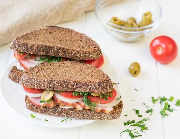 Sandwich au jambon fraîchement préparé sur une table en bois blanche.