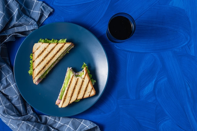 Sandwich au jambon et légumes verts sur fond bleu.