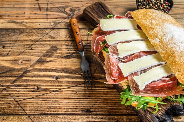 Sandwich au jambon de Parme sur pain ciabatta avec roquette et camembert brie. fond en bois. Vue de dessus. Espace de copie.