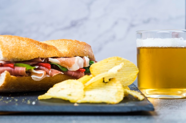 Sandwich au jambon serrano avec piquillos servi sur une assiette en ardoise avec frites