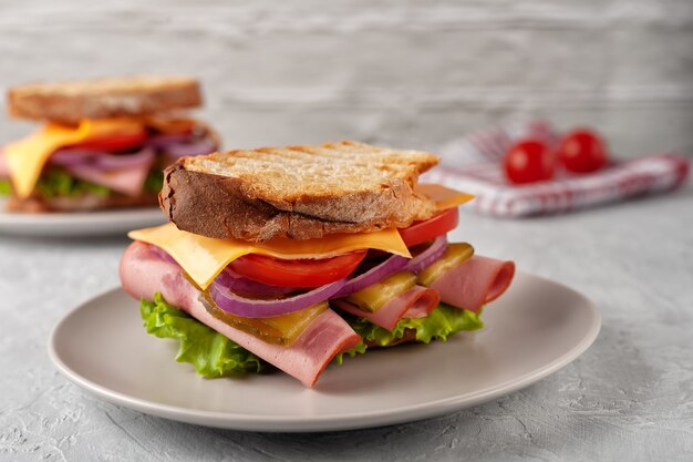 Sandwich au jambon, tomates, laitue et fromage jaune sur fond gris