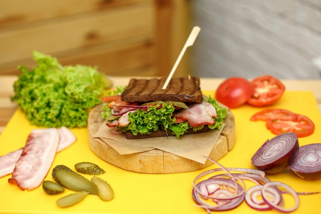 Sandwich au pain noir grillé sur une plaque en bois sur un plateau jaune