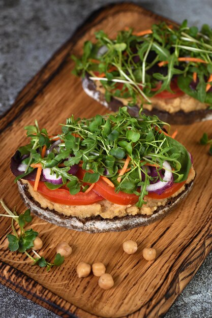 Sandwich au pain rustique grillé avec houmous de pois chiches, tranches de tomates, mélange de laitue et micro-pousses. Petit-déjeuner végétarien.