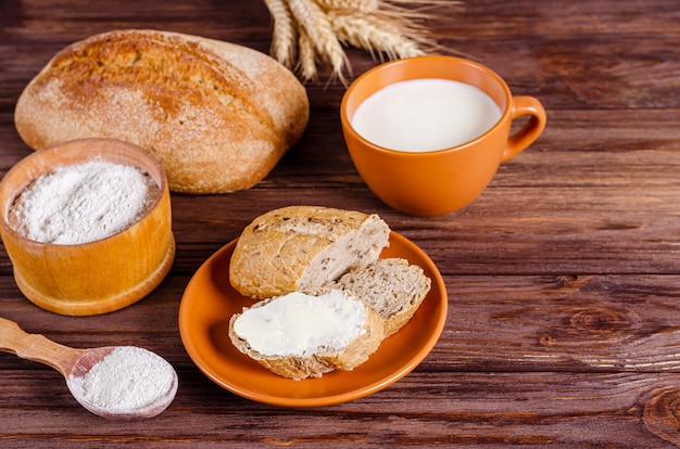 Photo sandwich au pain de seigle avec petit crémeux sur une assiette et une tasse de lait sur une surface en bois