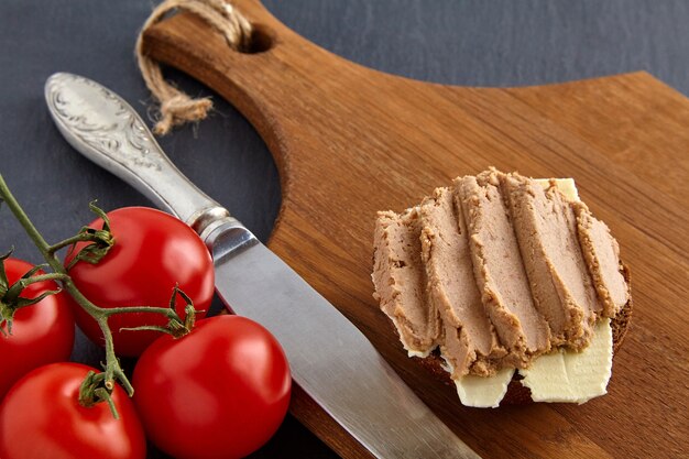 Sandwich au pâté fait maison sur planche de bois sur table noire en pierre avec tomates cerises et couteau de cuisine